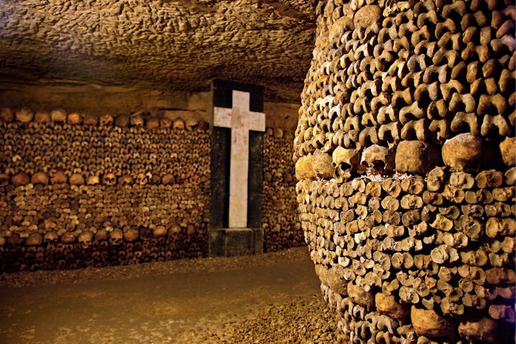 An ossuary is full of skeletal remains forming a pillar and lining the walls – with a large white cross in the centre of a back wall.