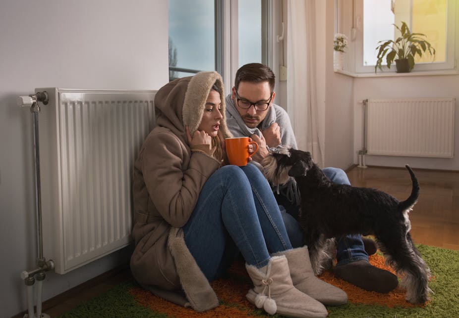 A man a woman sat on the floor next to a radiator with their dog trying to stay warm