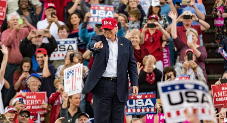 A man in a red cap points to the crowd.