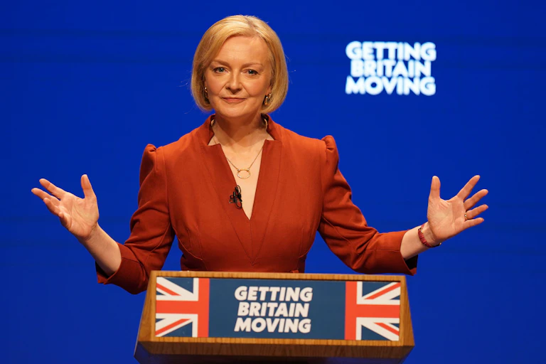 A lady in a red dress at a lectern against a blue background.