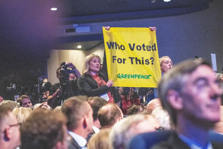 Protestors in a crowd hold up a yellow banner.