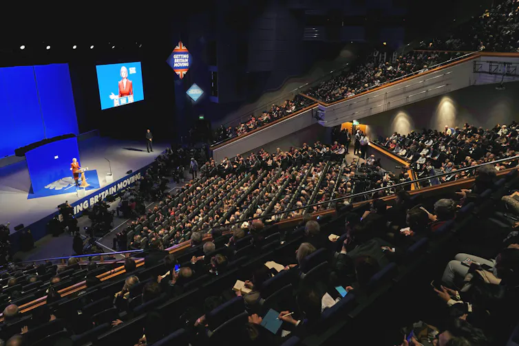 A crowd in an auditorium watch someone on stage.