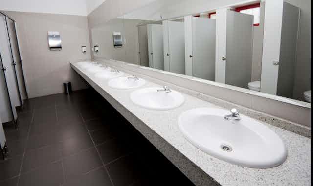 A row of sinks and bathroom stalls in a public bathroom.