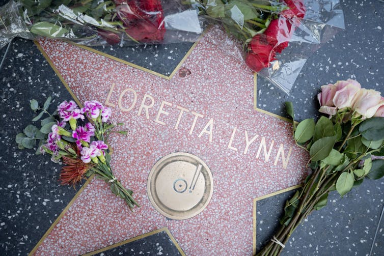 A star engraved in sidewalk pavement surrounded by bouquets of flowers.