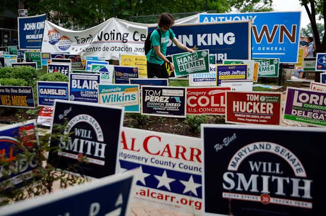 At least two dozen candidate campaign signs stuck in the ground next to a voting place. 