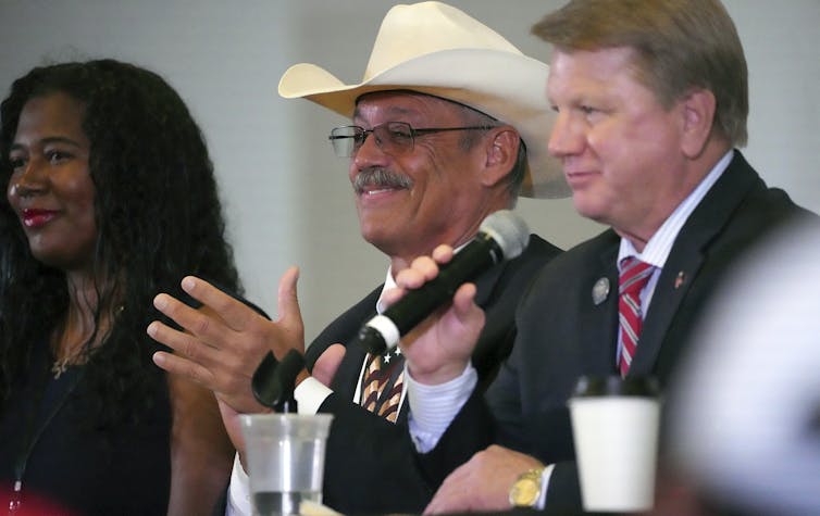 A young woman and two middle-aged men, one wearing a cowboy hat, sit at a table.