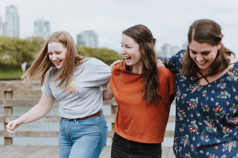 Three young women laughing while walking together, linking arms