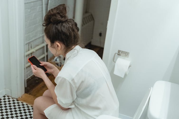 A woman sits on the toilet.