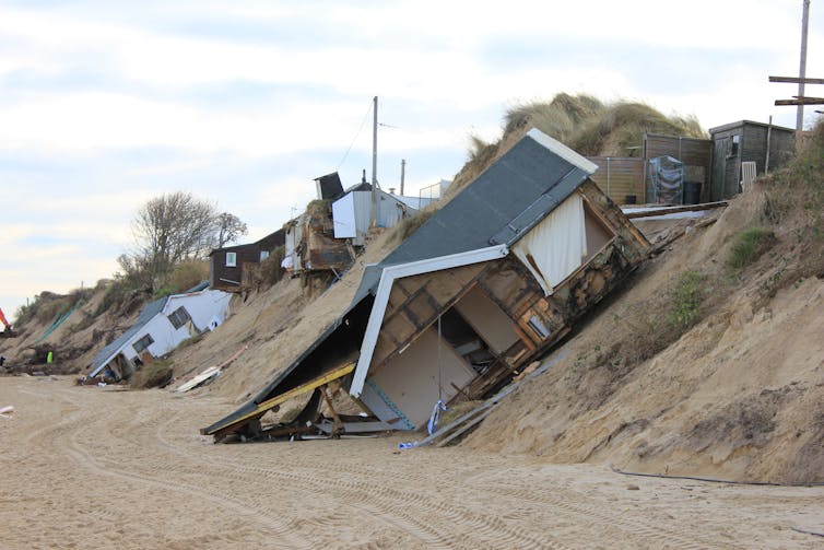 A series of collapsed houses along a sandy outcrop.