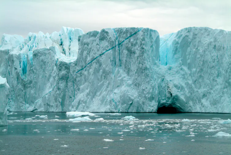 A vast wall of blue and white ice with ocean in the foreground.