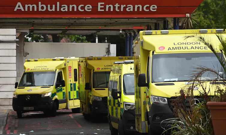 A number of ambulances waiting under a sign 'Ambulance Entrance'.