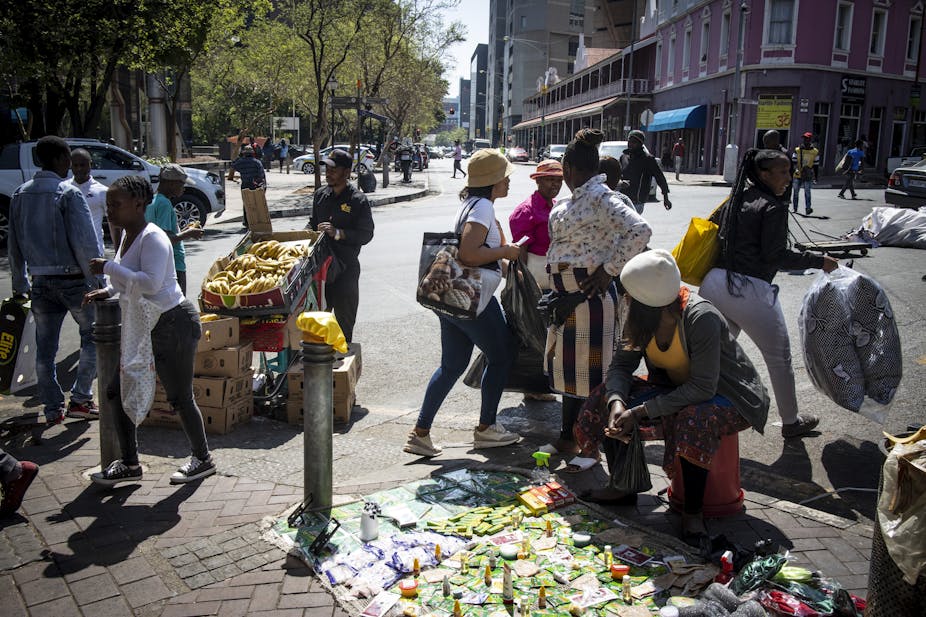 A woman displays her wares for sale on a Johannesburg street while a man stands next to his shopping trolley filled with bananas. 