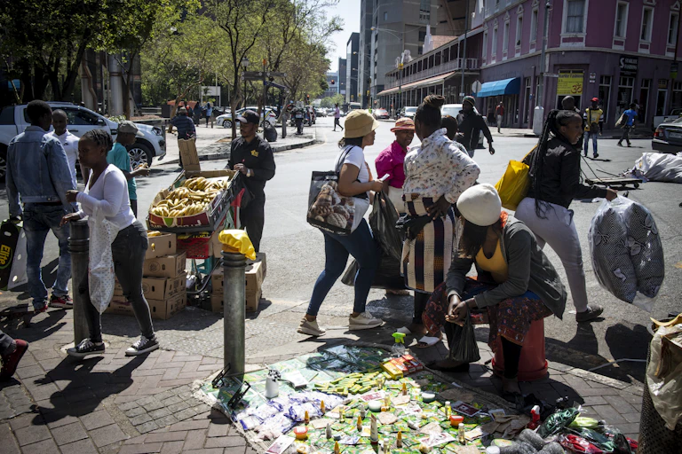 A woman displays her wares for sale on a Johannesburg street while a man stands next to his shopping trolley filled with bananas.