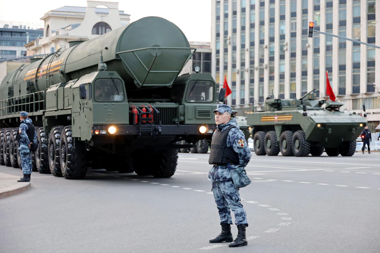 A Russian soldier stands in the street as a strategic nuclear warhead passes in the background.