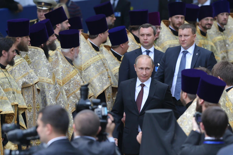 Men in suits walk through a line of religious figures.
