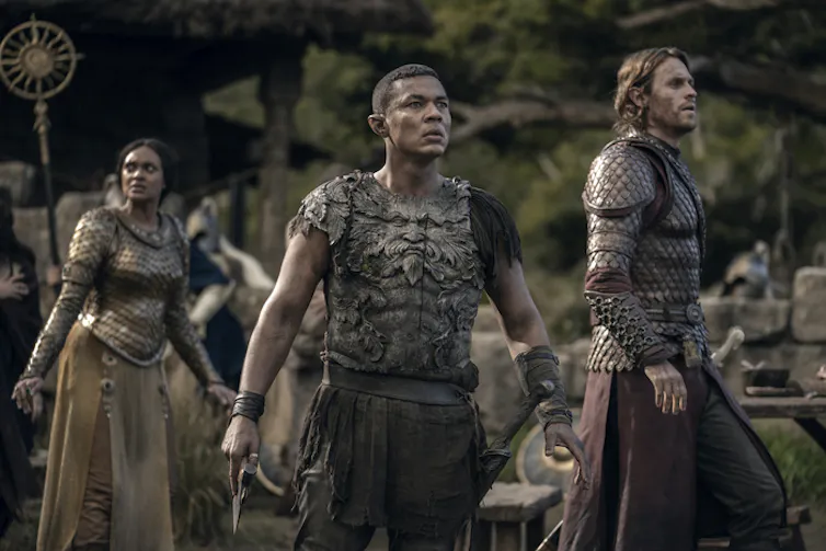 An elf looking watchful and alert with pointed ears in body armour stares into the distance flanked by two other figures.