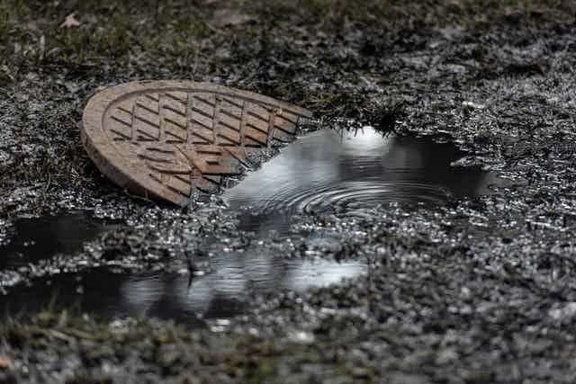 Dark liquid wells up around a tilted manhole cover