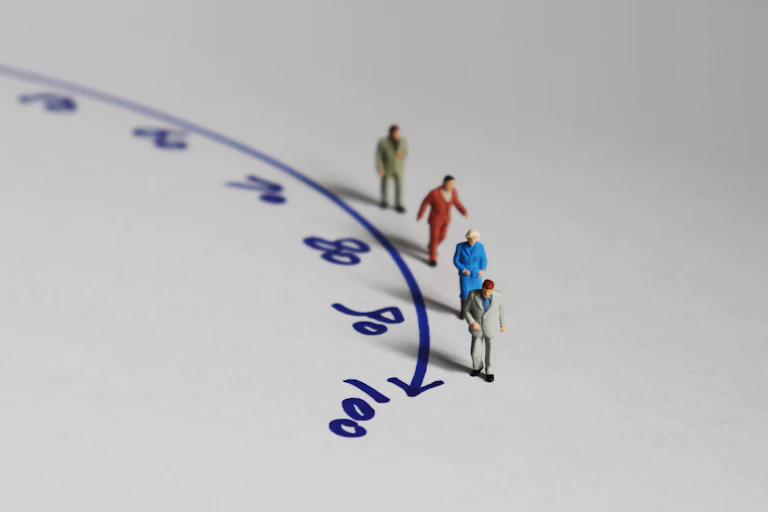 Minature people walking along a curved arrow with numbers denoting different ages.