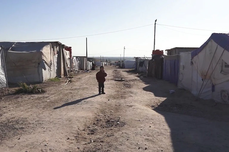 child stands in dusty detention camp