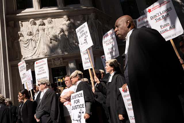 Barristers in black robes and wigs hold up protest placards.