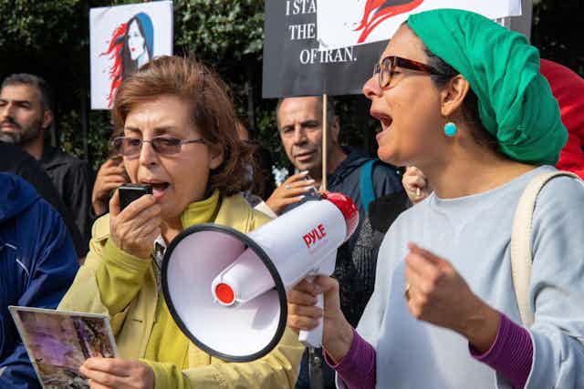 Two women, one carrying a megaphone and wearing a green headscarf at a protest.