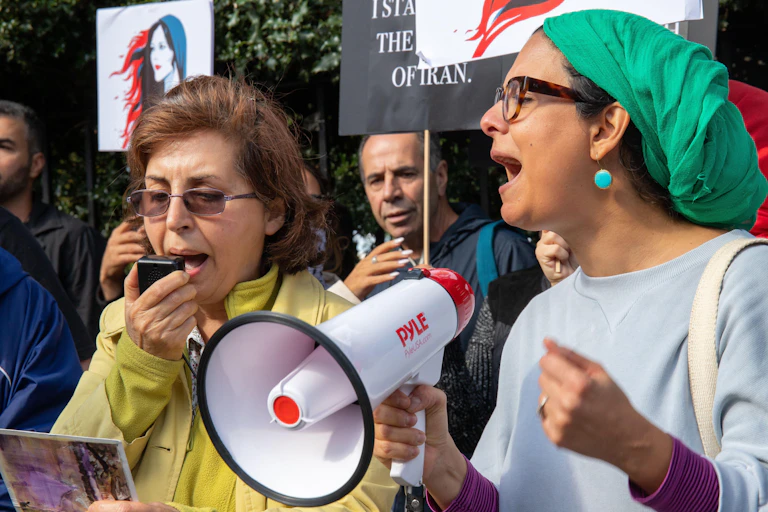 Two women, one carrying a megaphone and wearing a green headscarf at a protest.