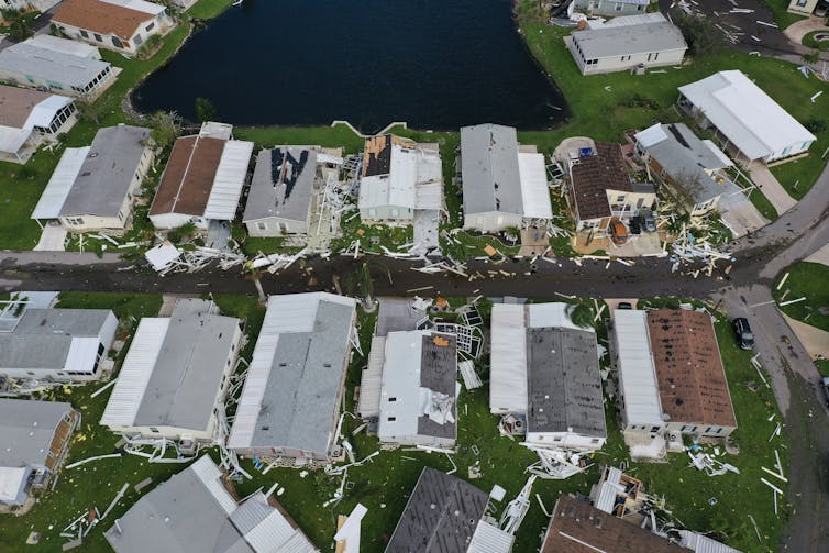 Rows of closely spaced houses next to an inlet or lake.  Many have apparently damaged roofs.