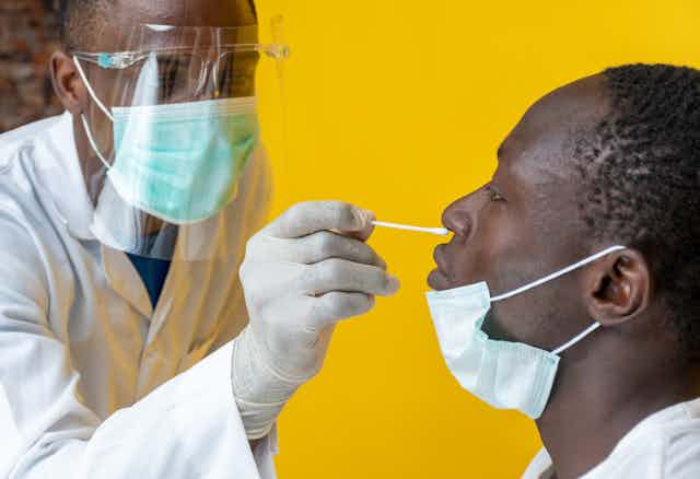 Un jeune médecin africain fait un prélèvement nasal à un homme noir.
