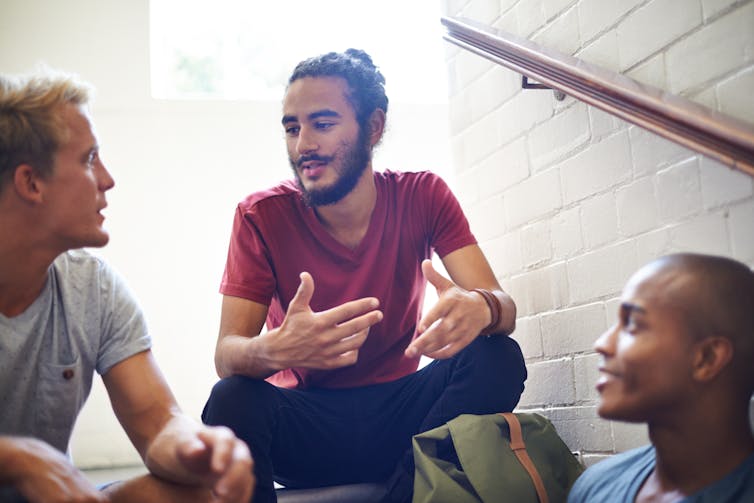 Three young men sitting on a staircase talking.