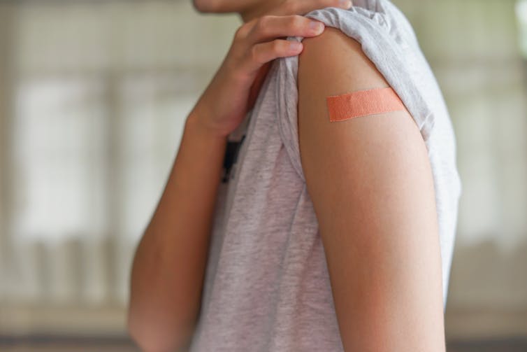 A person shows their upper arm, covered with a small bandage after vaccination