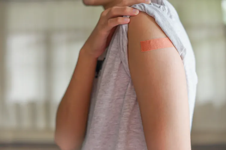 Une personne montre le haut de son bras, couvert d’un petit pansement après vaccination