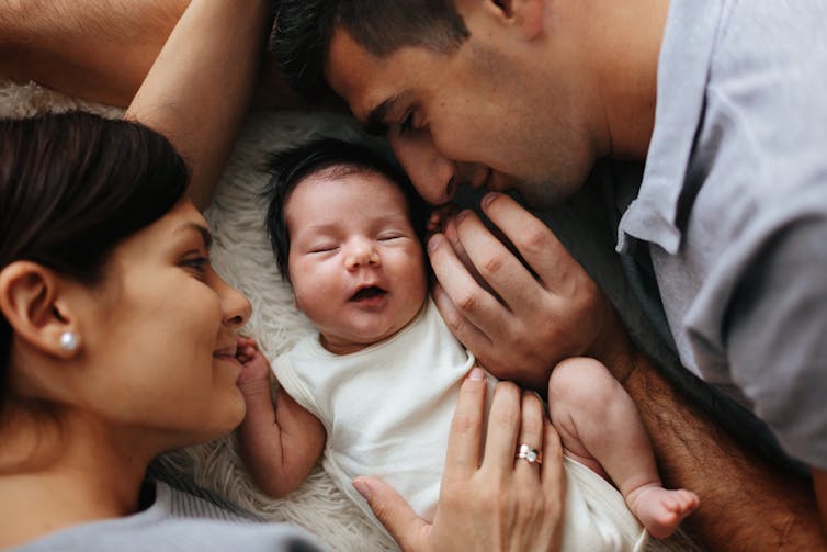 A couple frame a newborn baby with their hands and faces