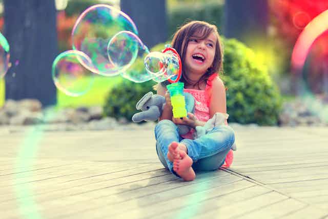 A little girl smiling against a colourful background with big colourful bubbles.