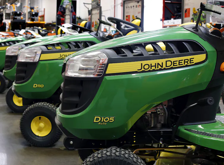 Green John Deere branded drivable lawn mowers sit on display.
