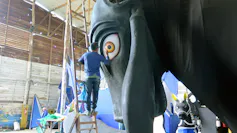 A man standing next to a large sculpture of a horse painting the horse's eye.