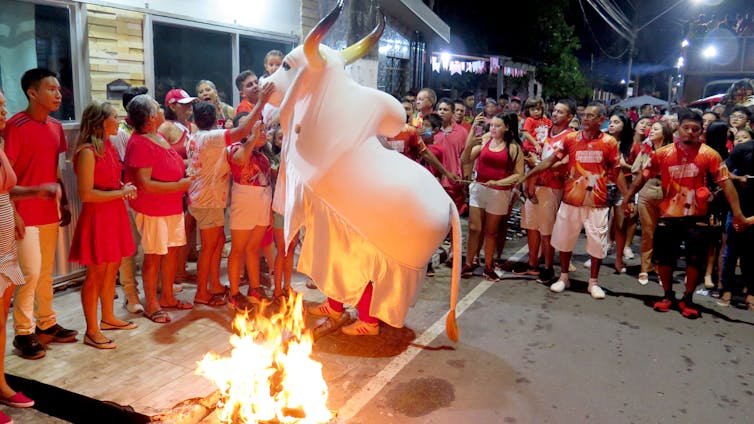A group of people wearing red shirts gather around a bonfire and a fake cow with horns.