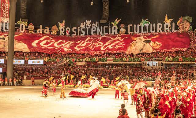 A stadium filled with people. Performers in red costumes are seen in the foreground.