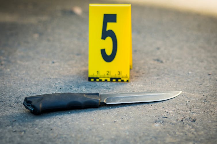 A knife on the ground with the number five on a yellow card in the background