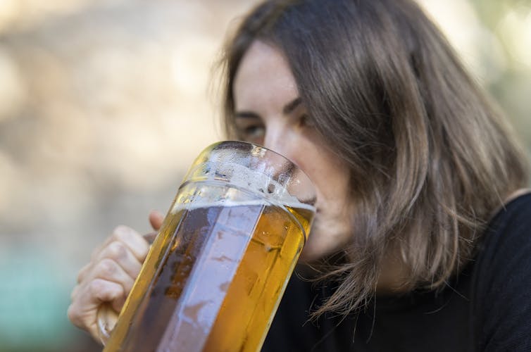 A woman drinks beer outdoors.