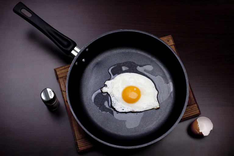 A black, non-stick pan is used to fry an egg.