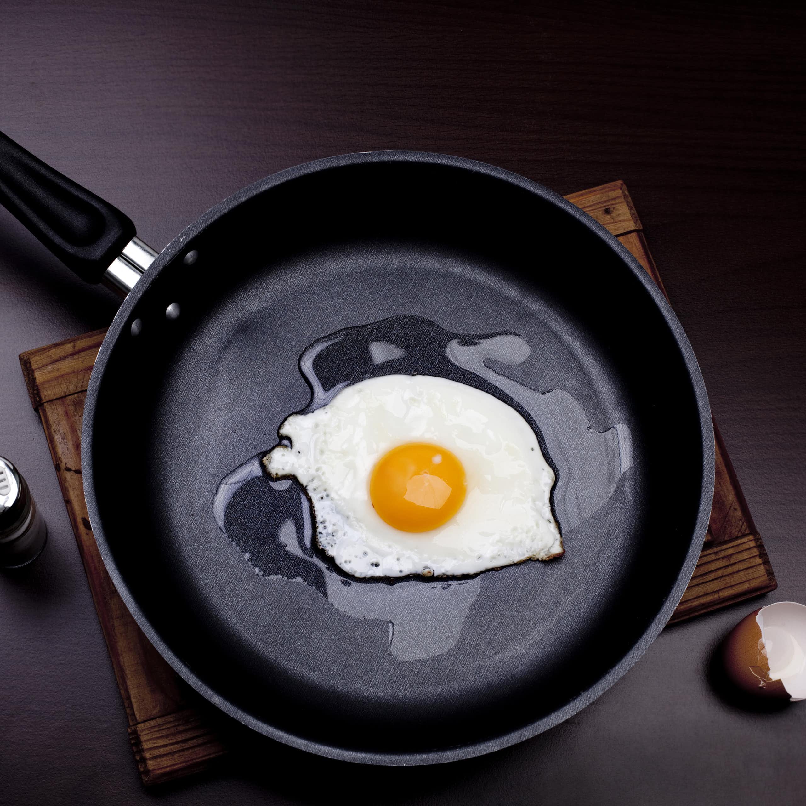 A black, non-stick pan is used to fry an egg.