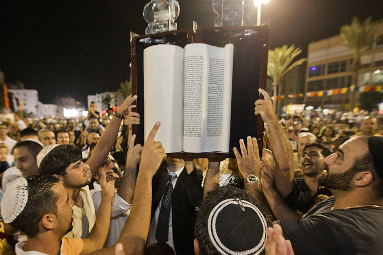 Men in a crowd gather around a large book held above their heads.