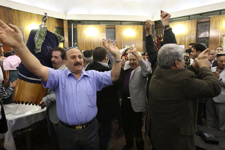 A handful of men dance with their hands in the air, as one of them holds a covered Torah scroll.