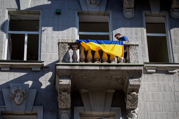 Мужчина стоит на балконе разрушенного дома рядом с украинским флагом после ракетного обстрела Россией центра Киева.