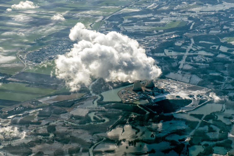 An aerial view of a nuclear power plant surrounded by pools of water with a large cloud of steam drifting through the sky.