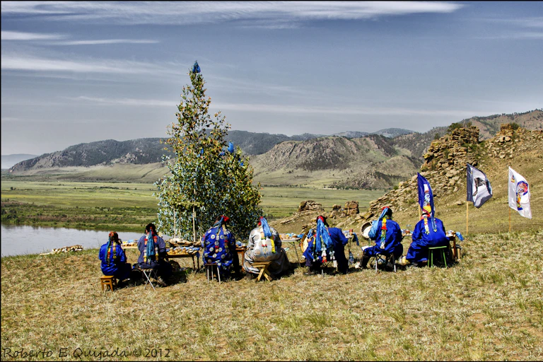People sitting in a row with their heads bent, while facing the mountains ahead of them.