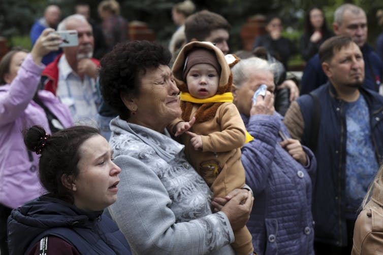 An aging woman with dark hair weeps as she holds a baby.