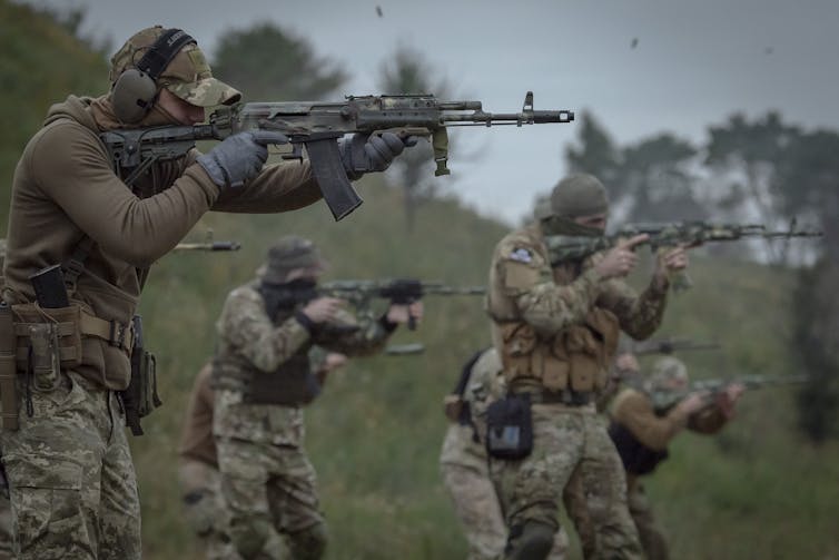Men wearing camouflage hold weapons as they do military drills in a field.