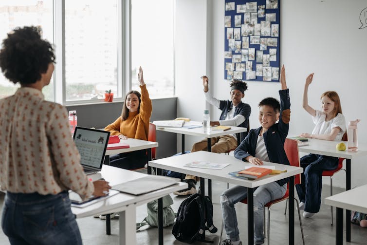 Teen students in a class, some with raised hands.