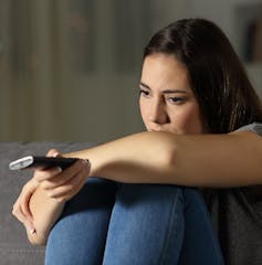 A teen watching television looking glum.